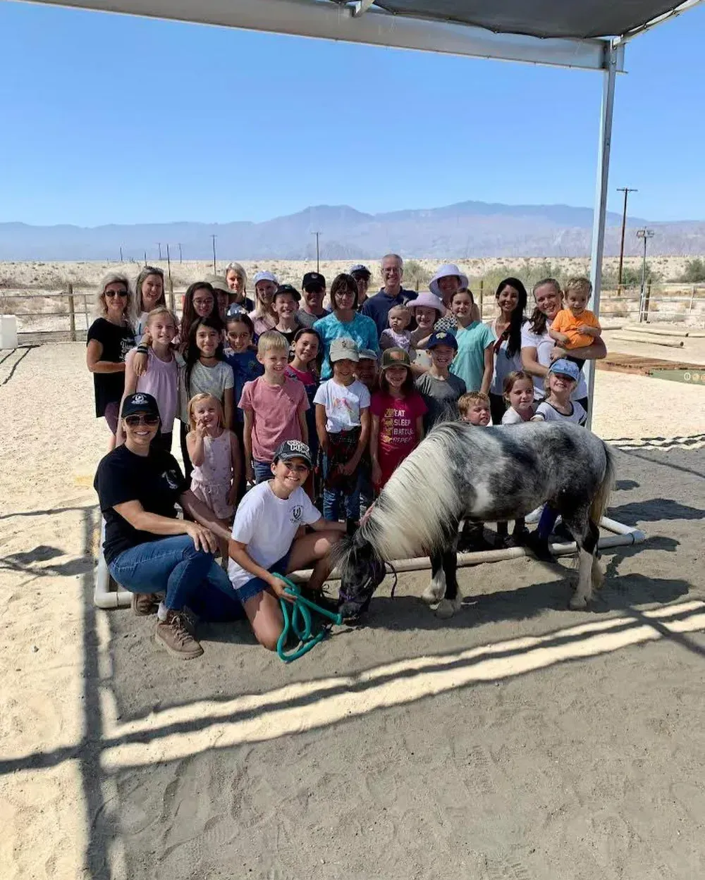 A group of families and children posing with a pony under a shade shelter at Coachella Valley Horse Rescue